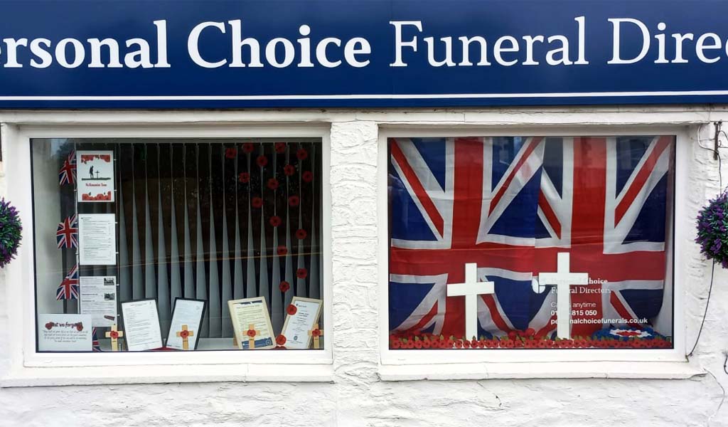 Personal Choice Funeral Directors Remembrance Day window display for their Par branch. It has union jack flags in the window with white crosses on the bottom of the window.
